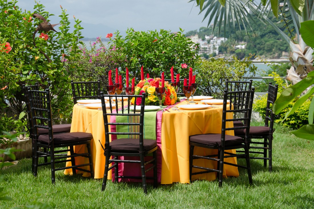 A table setting on a garden, with yellow linen, and black chairs.